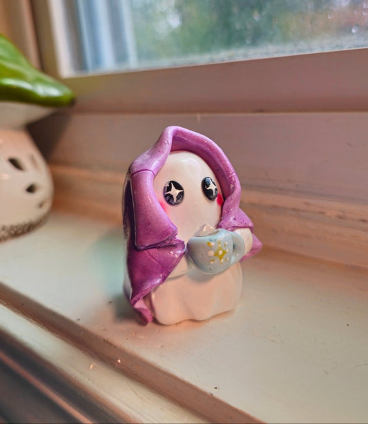 Small figurine ghost with a blanket draped over her with a cup of cocoa