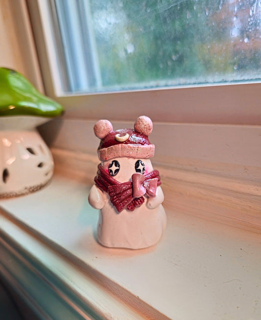 Small figurine wearing a pink hat and scarf on a windowsill with a rainy day view outside.