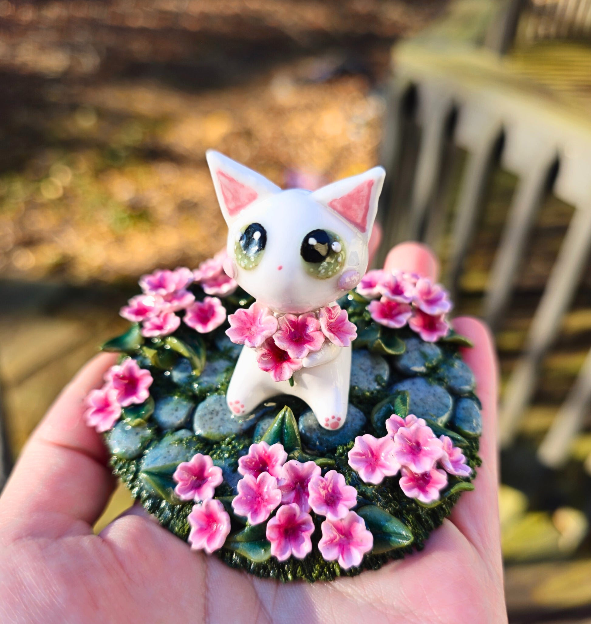 White cat figurine with pink flowers on a decorative stone base held in a hand.