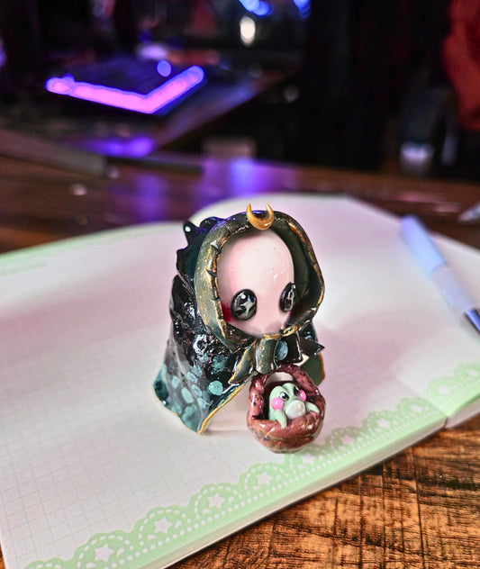 small decorative figurine of a magical ghost with babushka hood, holding a basket with a frog in it