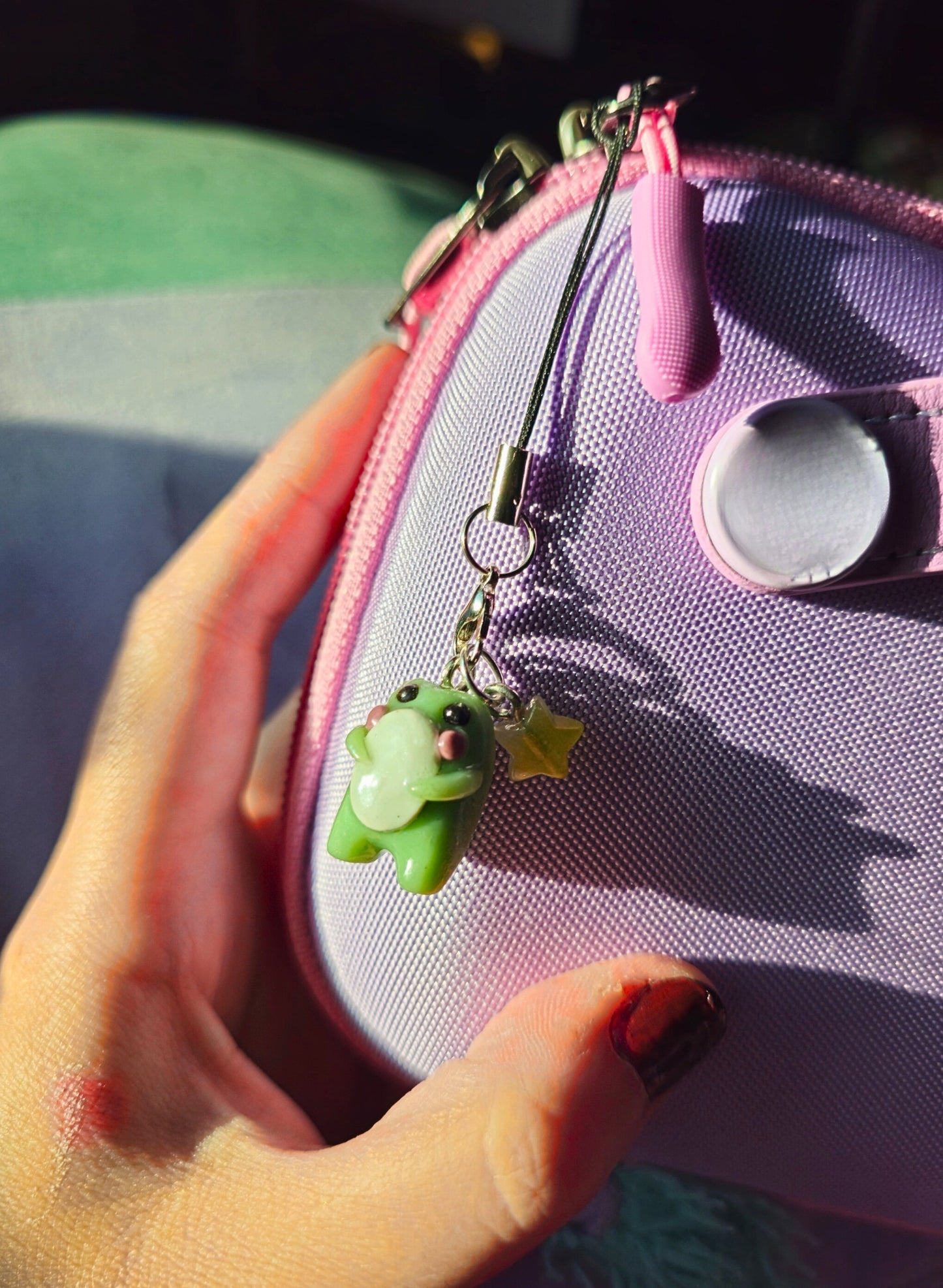 Purple pouch with a green frog charm held by a hand