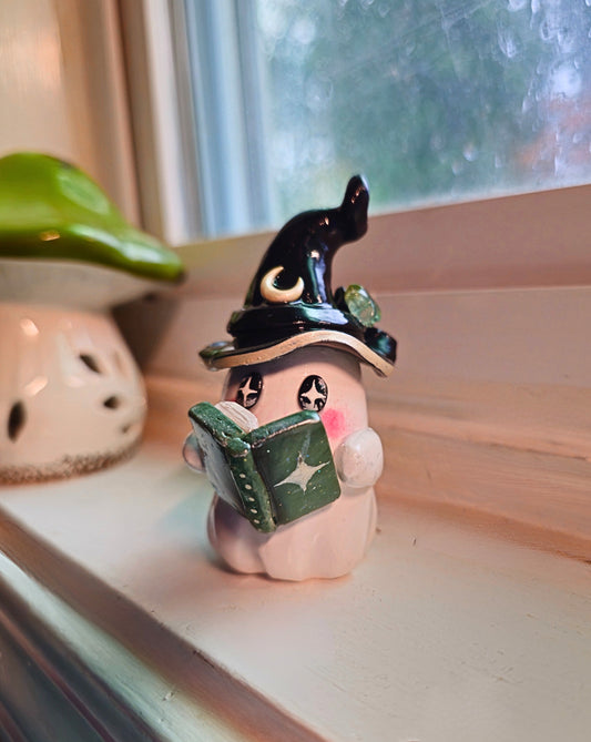 Small figurine of a witch ghost reading a book on a windowsill.